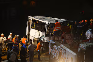 A damaged tour bus on the roadside near a crash scene in the Dominican Republic with emergency responders and onlookers
