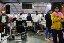 Travelers check digital flight information boards showing widespread cancellations at an international airport as global airlines suspend schedules due to airspace closures linked to the U.S.–Iran conflict.